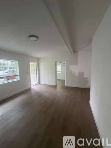 A room with wooden floors and white walls, with a window on the left side.