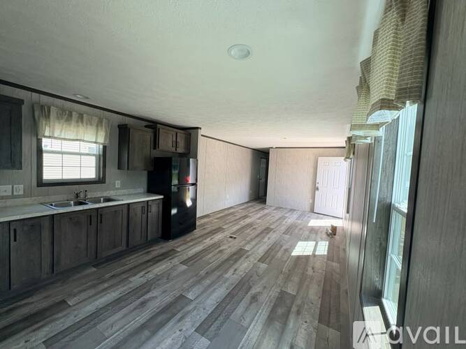 A living room with wood flooring and a kitchen area to the left.