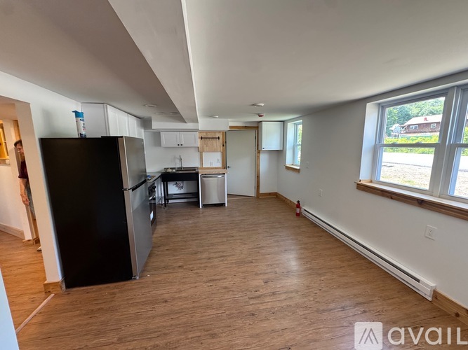 A kitchen area with a black fridge, white cabinets, and a wooden floor.