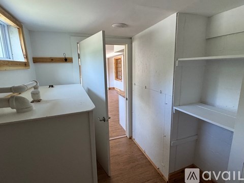 A white kitchen with a sink and a doorway leading to another room.
