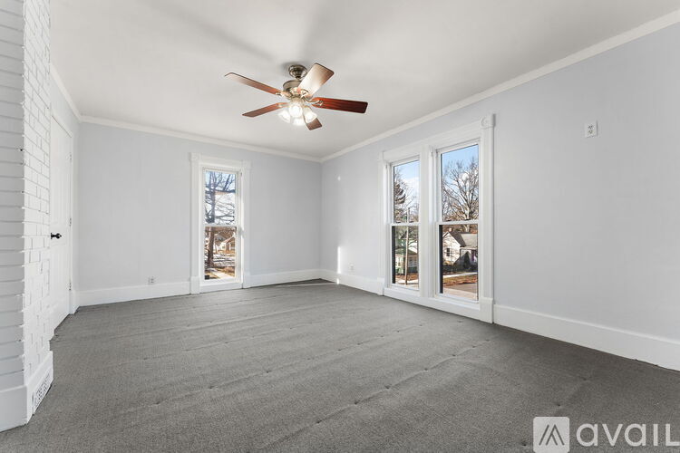 A spacious room with a ceiling fan and two windows.