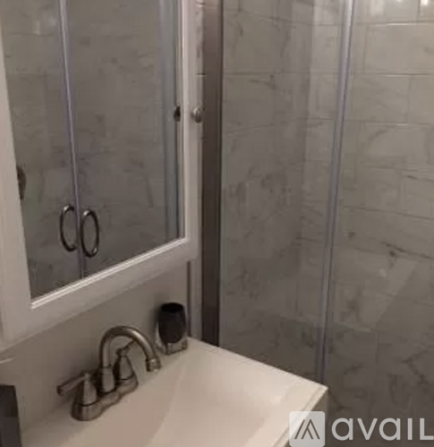A bathroom sink with a white counter top and a glass shower door.