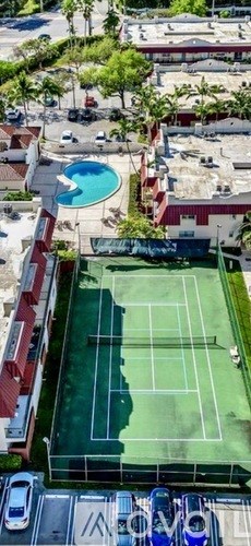 Tennis court surrounded by a pool and trees.