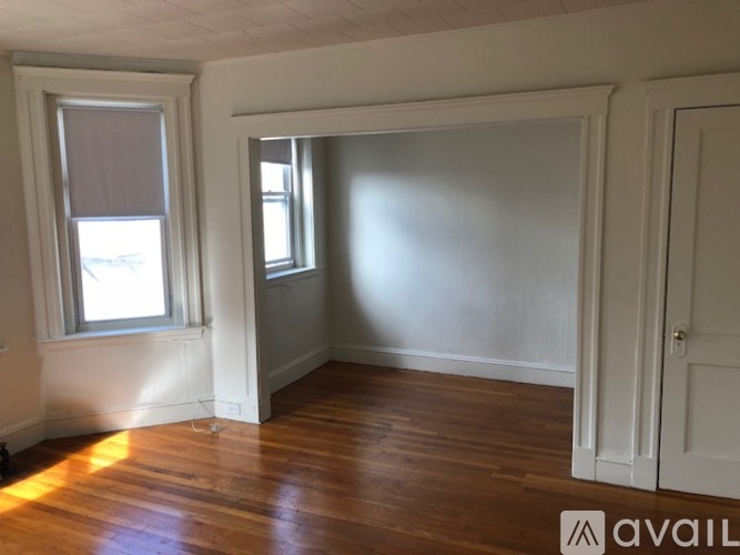 A room with wooden floors and white walls, with a window on the left and a door on the right.
