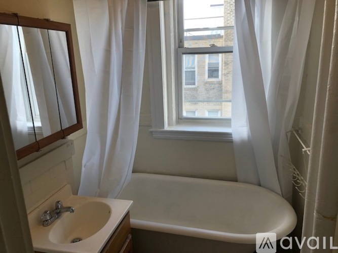 A bathroom with a white tub, sink, and curtains.