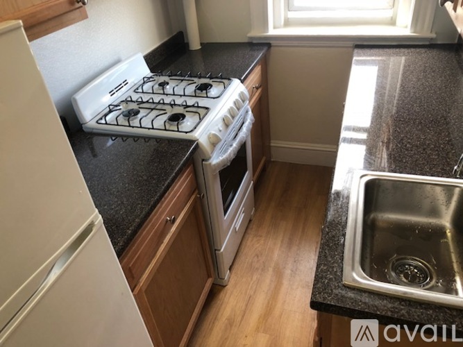 A kitchen with a white fridge, a black countertop, and a stainless steel sink.