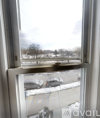 A view from a window looking out to a snowy landscape with cars parked in the distance.