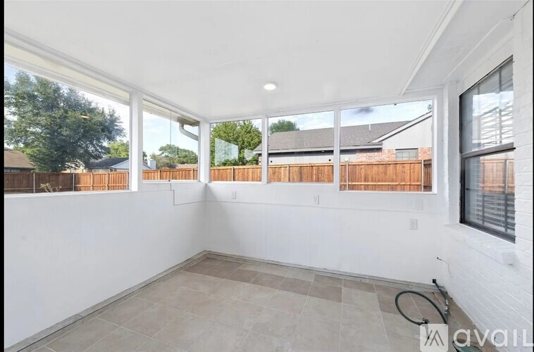 A room with white walls and a tiled floor with a view of a fence and trees outside.