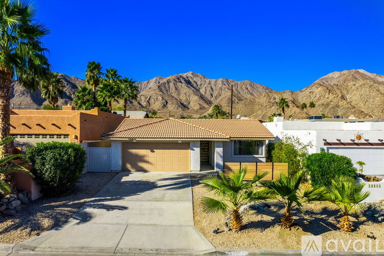 A house with a brown roof and a white garage door is surrounded by palm trees.