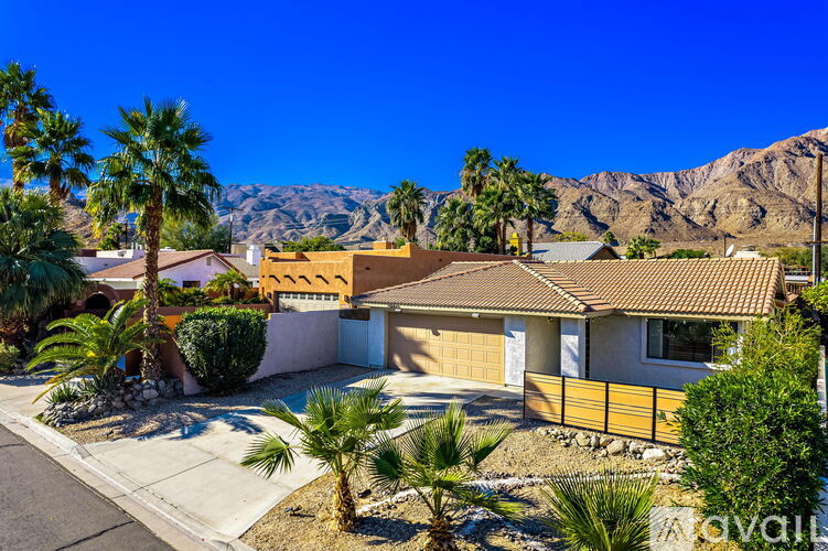 A house with a brown roof and a white garage door is surrounded by palm trees.