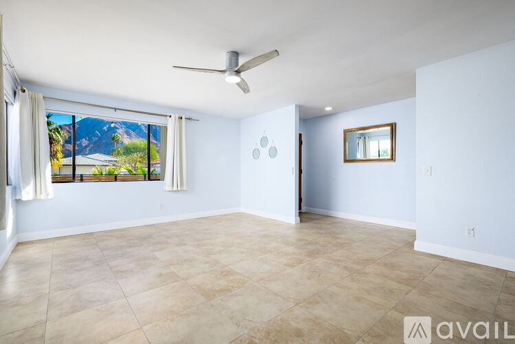 A spacious room with a ceiling fan and a large window overlooking a mountainous landscape.