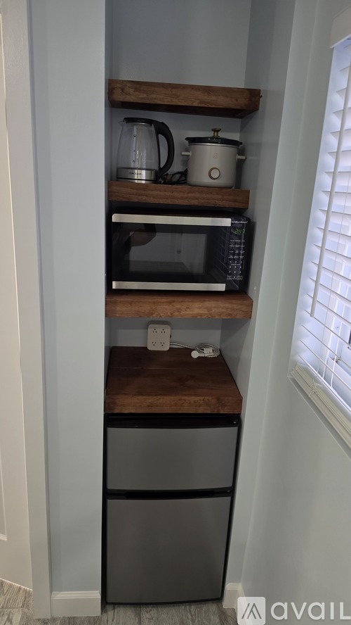 A kitchen with a microwave, kettle, and pot on a shelf above a dishwasher.