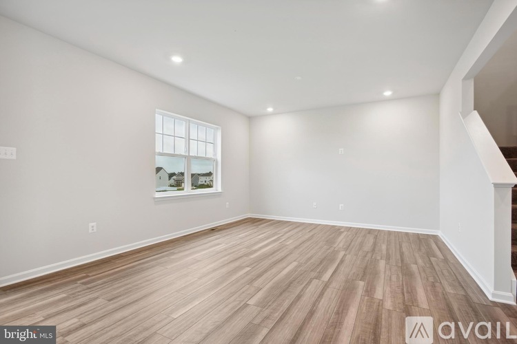 A spacious room with wooden flooring and a window showing a view of other buildings.