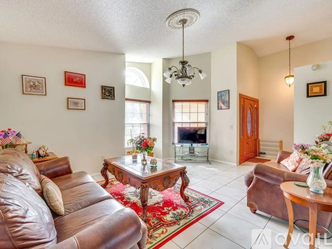 A living room with a brown leather couch and a chandelier hanging from the ceiling.