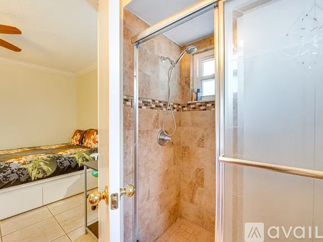 A bathroom with a glass shower door and a bedroom with a bed and a ceiling fan.