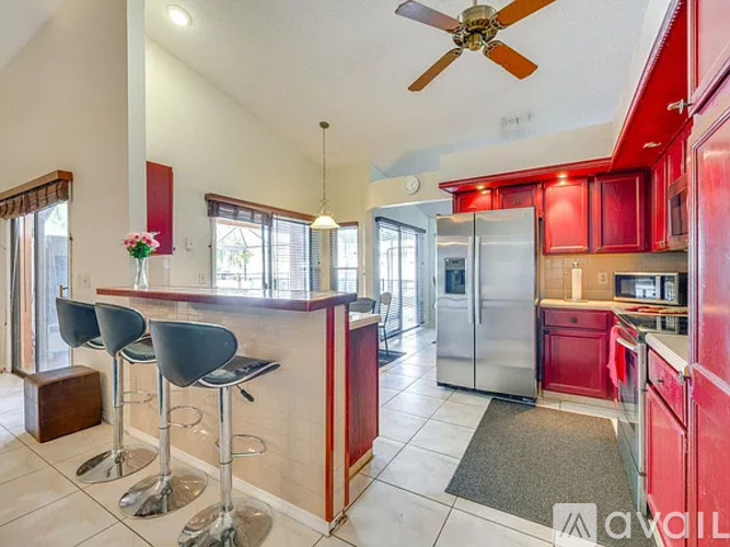 A kitchen with red cabinets and a bar area with two stools.