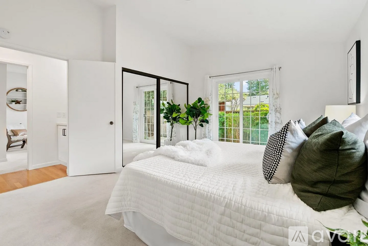 A white bedroom with a large bed and a view of the backyard.
