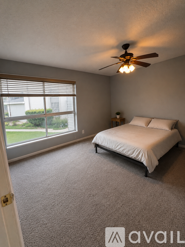 A bedroom with a bed, a window with blinds, and a ceiling fan.