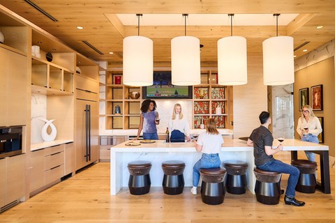 A group of people are sitting and standing around a table in a modern kitchen.