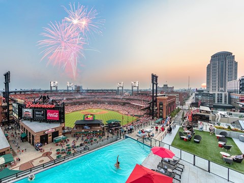 A fireworks display over a baseball stadium with a pool in the foreground.