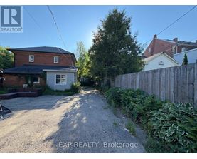 A gravel driveway leads to a house with a white fence and green plants on the side.