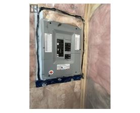 A wall-mounted electrical box with a grey exterior and a black interior is installed in a wall covered with insulation material.