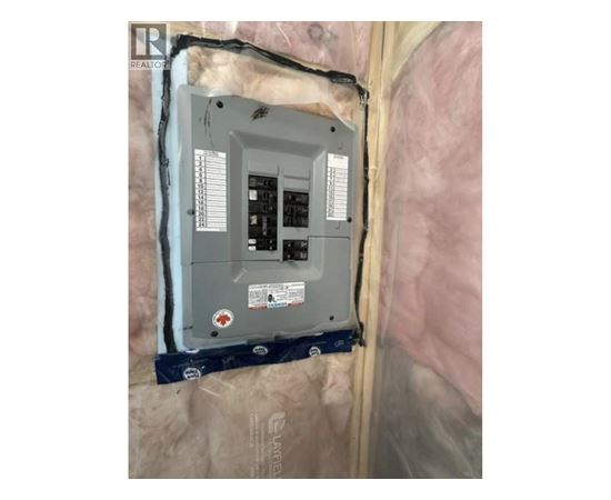 A wall-mounted electrical box with a grey exterior and a black interior is installed in a wall covered with insulation material.