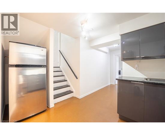 A modern kitchen with a stainless steel refrigerator and a staircase leading to the upper floor.
