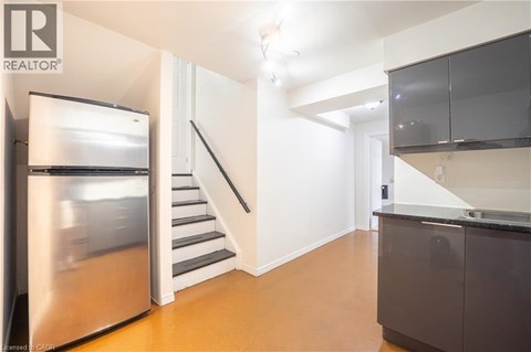 A modern kitchen with a stainless steel refrigerator and a staircase leading to the upper floor.