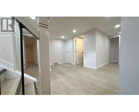 A spacious room with wooden flooring and white walls, with a staircase on the left side.