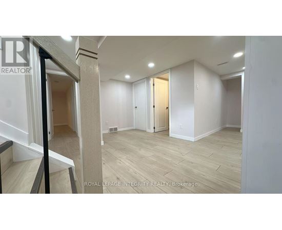 A spacious room with wooden flooring and white walls, with a staircase on the left side.