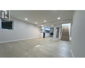 A spacious room with wooden flooring and a staircase in the background.