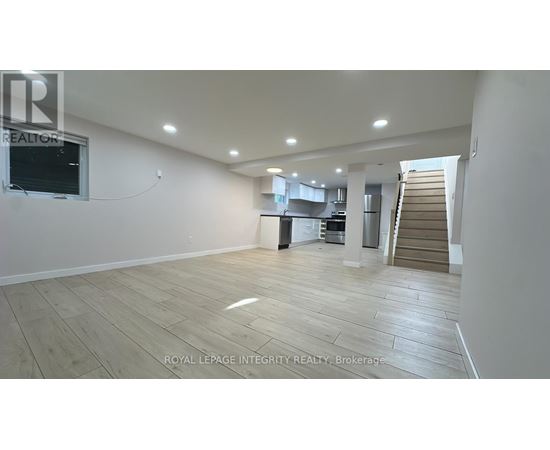 A spacious room with wooden flooring and a staircase in the background.