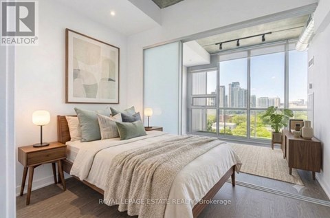 A bedroom with a large bed, a nightstand with a lamp, and a framed picture on the wall.