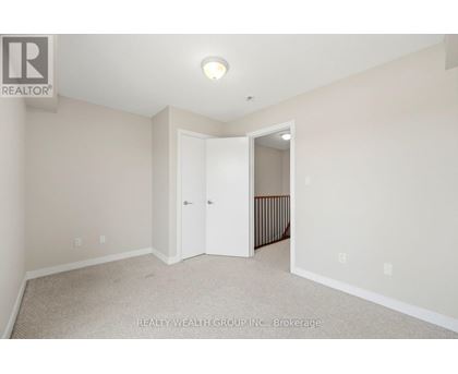 A white bedroom with a carpet floor and a doorway leading to a hallway.