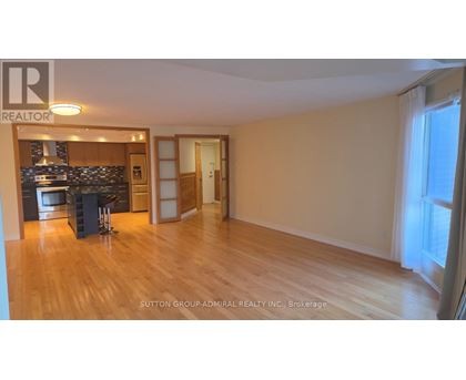 A spacious room with wooden flooring and a kitchen area with a stove and cabinets.