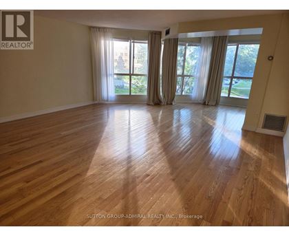 A spacious room with wooden flooring and large windows.