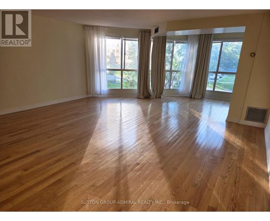 A spacious room with wooden flooring and large windows.