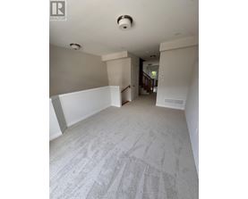 A spacious room with a carpeted floor and a staircase in the background.