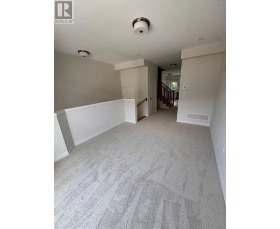 A spacious room with a carpeted floor and a staircase in the background.