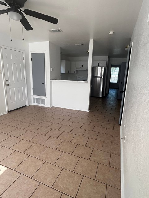 A kitchen area with a refrigerator, cabinets, and a ceiling fan.