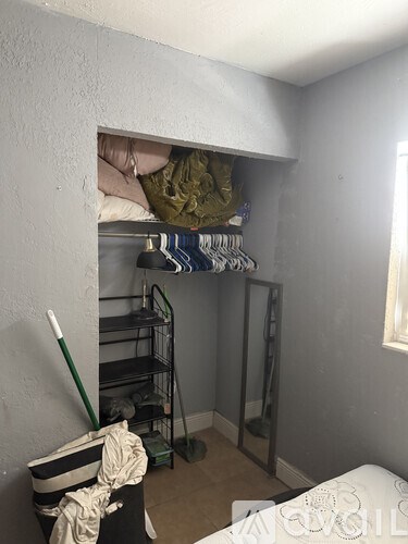 A small room with a bed and a closet with clothes hanging.