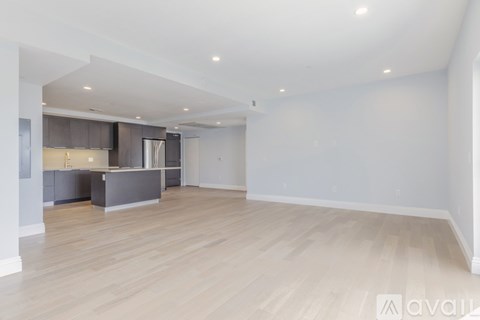 A spacious room with wooden flooring and a kitchen area in the background.