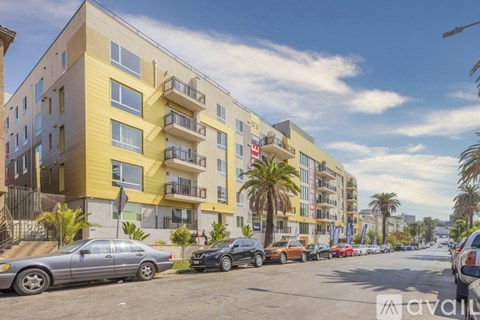 A street view of a residential area with cars parked on the side of the road and apartment buildings in the background.