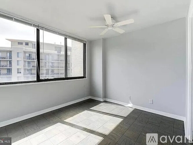 A room with a ceiling fan and large windows overlooking a building.