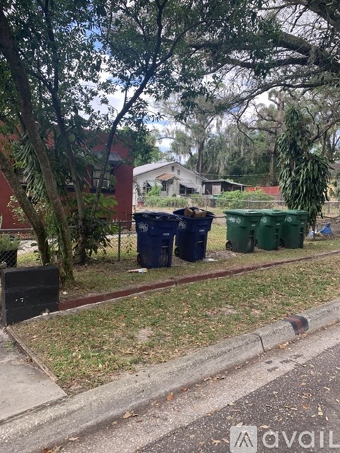 A green bin is on the grass next to a street.