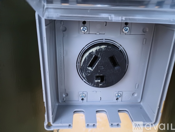 A grey electrical outlet box with a black plug in the center.