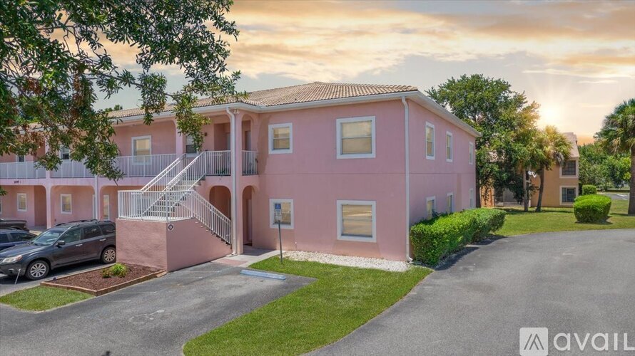 A pink house with a car parked in front and a driveway leading to the front door.