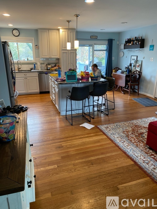 A woman is sitting at a kitchen island with a dining table and chairs around it.