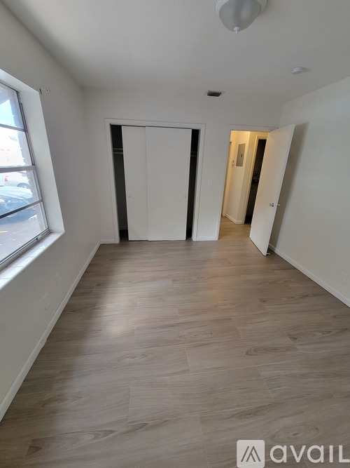 A room with wooden flooring and white walls, with a door on the left and another door on the right.